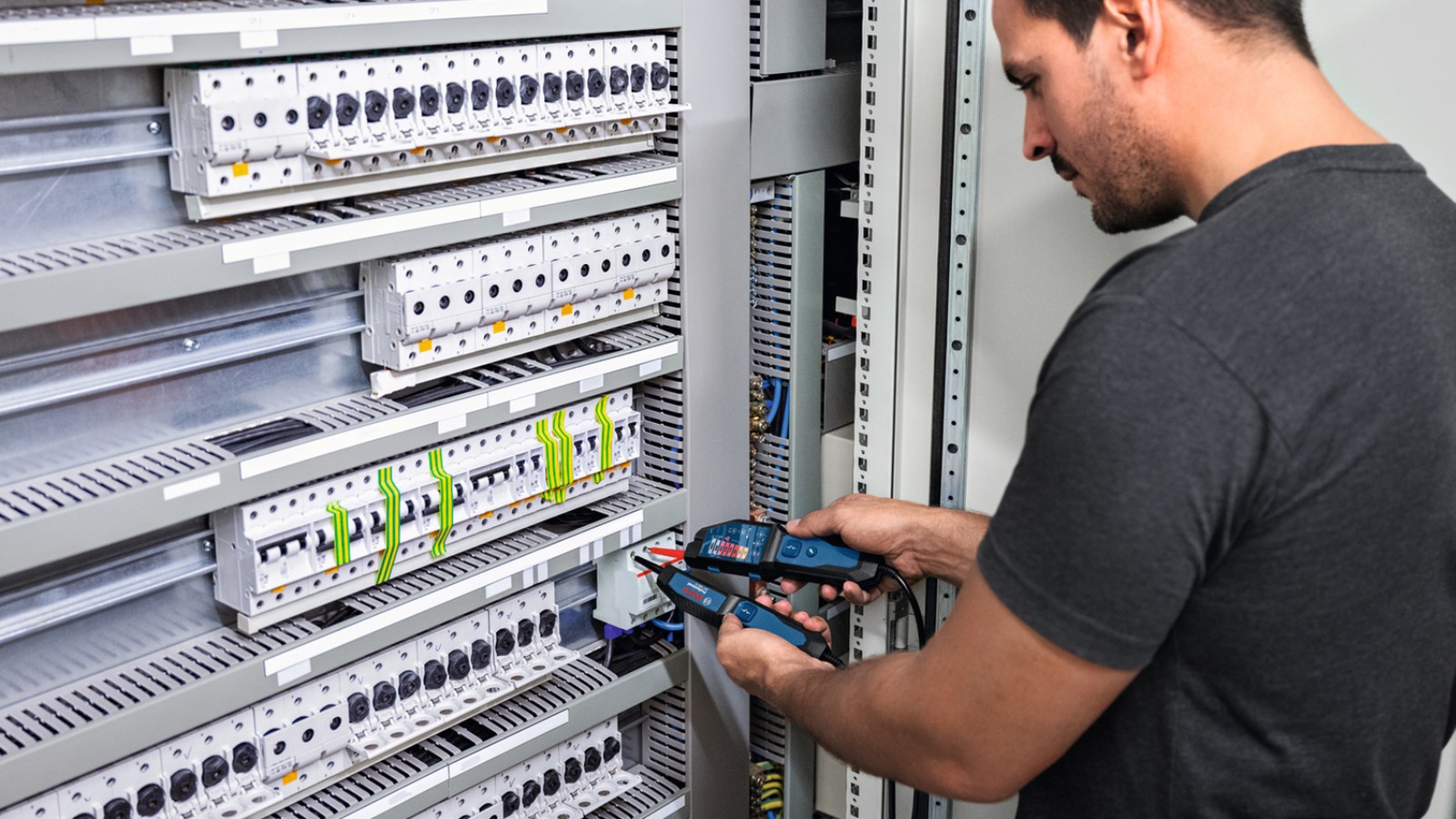 Elektryk mierzący pomiar elektryczności w szafie z bezpiecznikami.